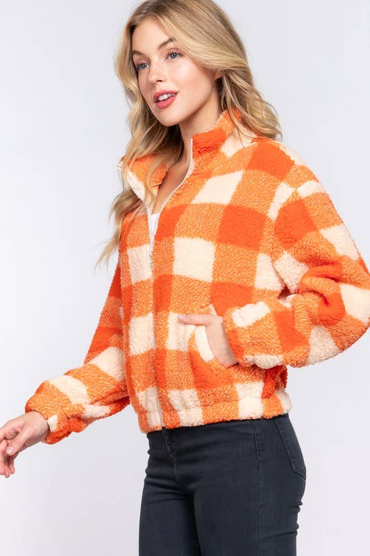 Woman wearing an orange and white checkered fleece jacket on a light gray background