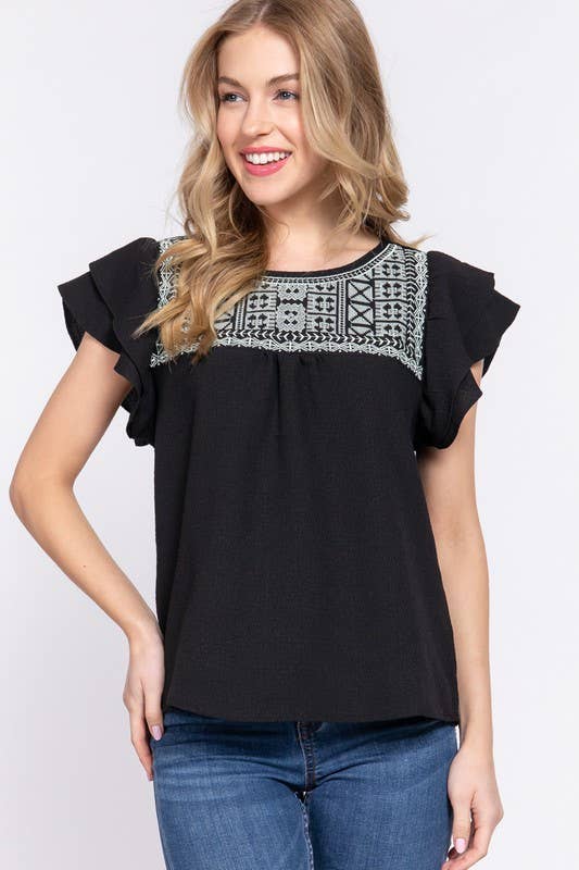 Woman wearing a black top with embroidery on a white background